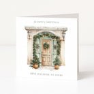 A square white Christmas greeting card standing upright on a white surface, featuring a watercolour-style illustration of a decorated front door with greenery and the text 'SEASON'S GREETINGS' and 'FROM OUR HOME TO YOURS'.