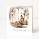 A square Christmas card with a watercolour illustration of a woman reading on a sofa by a window, with the text 'All is calm, all is bright' printed below, shown on a clean white background.
