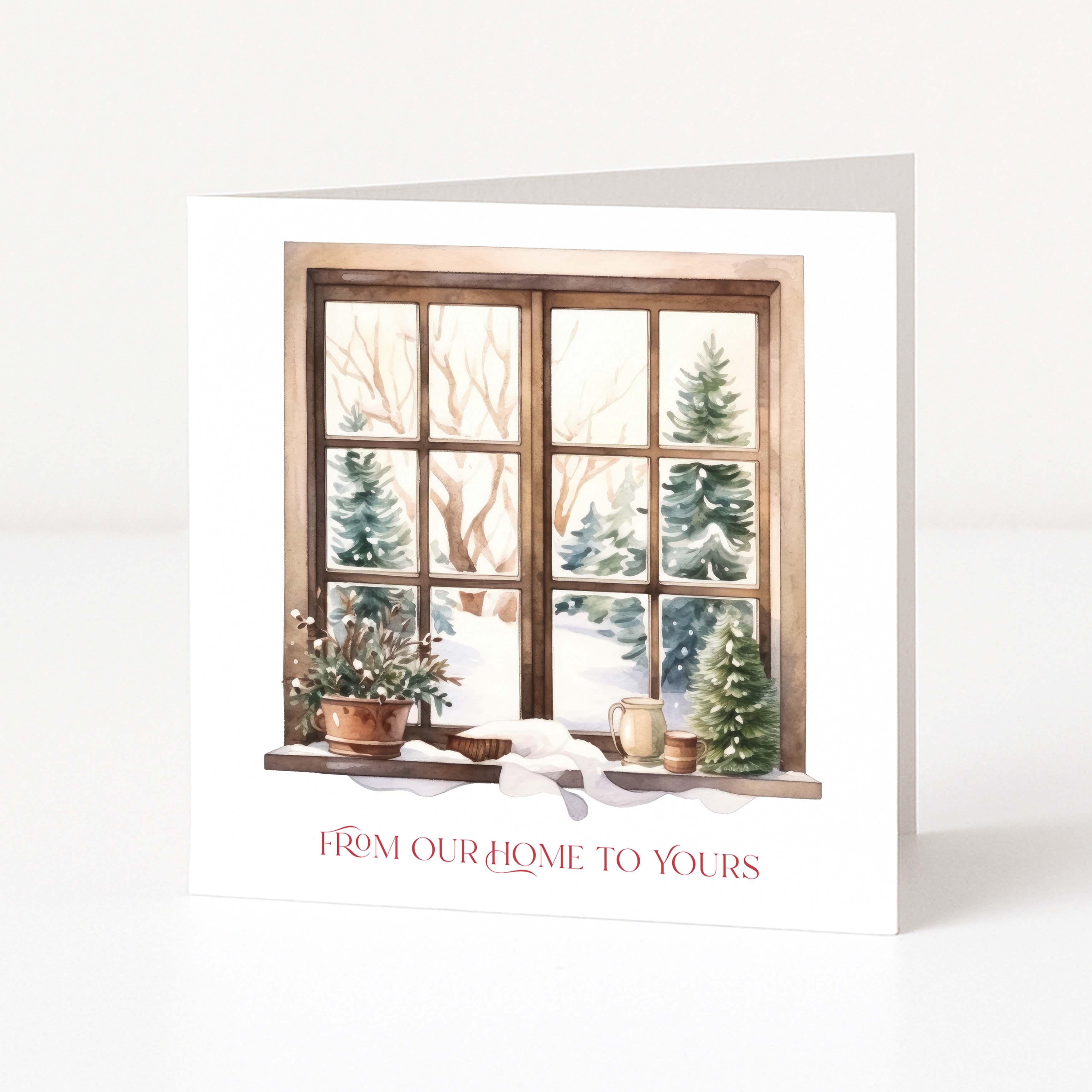 A white Christmas greeting card standing upright, printed with an illustration of a snowy window scene and the red text 'FROM OUR HOME TO YOURS' at the bottom, photographed on a clean white background.