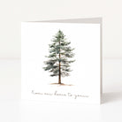 A white Christmas greeting card featuring a watercolour illustration of a snow-dusted pine tree and the printed phrase 'From our home to yours' in a delicate script at the bottom.