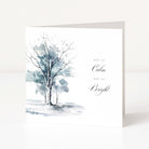 A white Christmas greeting card with a watercolour painting of two leafless trees in soft blue-grey tones and the words 'all is Calm all is Bright' in black script, shown standing against a white background.