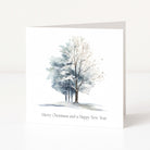 A square white Christmas greeting card standing upright on a white surface, featuring a watercolour winter tree illustration in soft blue, grey, and white tones, with the text 'Merry Christmas and a Happy New Year' printed below.