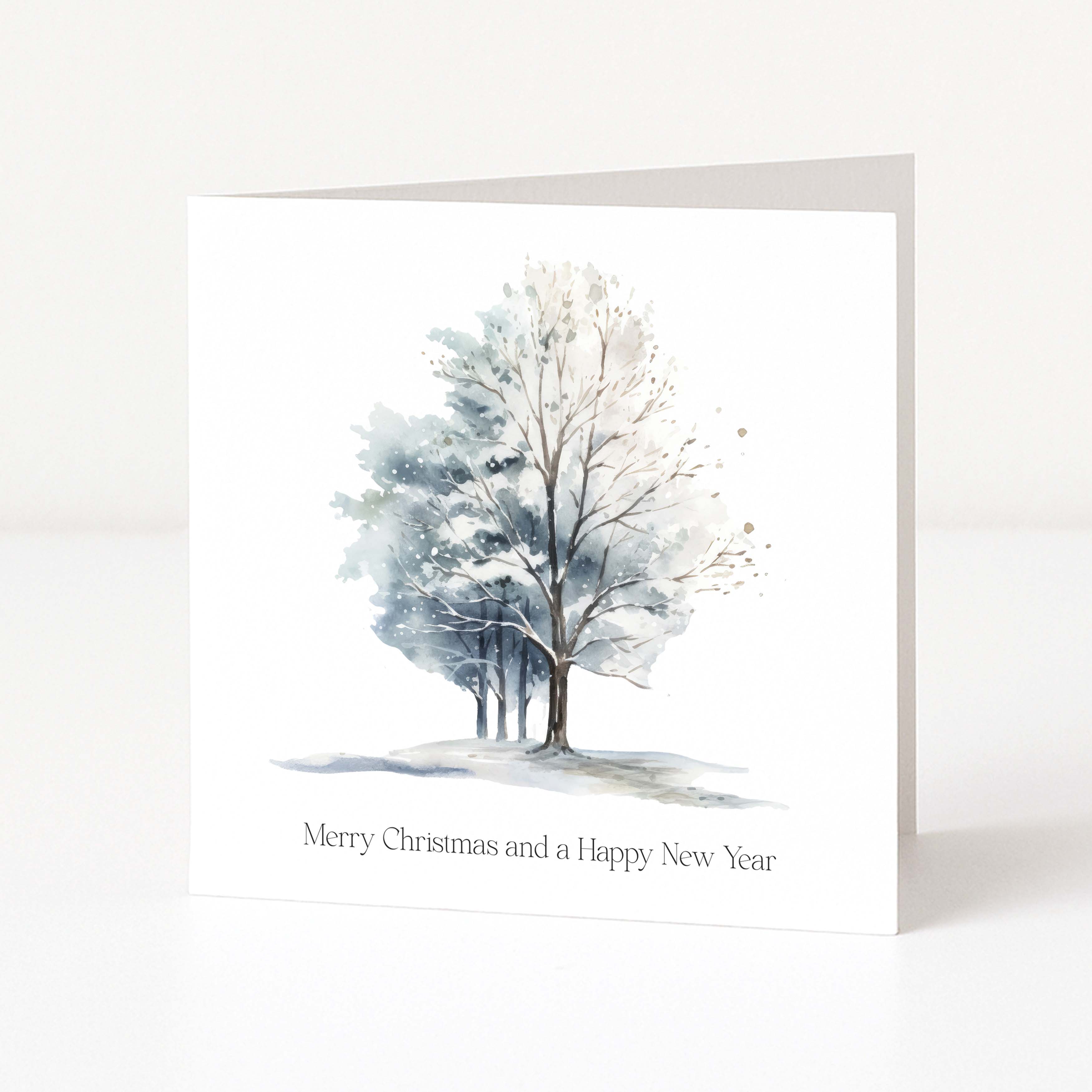 A square white Christmas greeting card standing upright on a white surface, featuring a watercolour winter tree illustration in soft blue, grey, and white tones, with the text 'Merry Christmas and a Happy New Year' printed below.