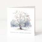 A square white Christmas greeting card standing upright on a white surface, featuring a watercolour winter tree scene in soft grey, blue, and beige tones, with the text 'WISHING YOU A MERRY CHRISTMAS' printed near the bottom.