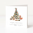 A white square Christmas greeting card standing upright on a white surface, featuring a watercolour-style Christmas tree with ornaments, wrapped gifts, a small train, and a fox. The text reads 'MERRY CHRISTMAS and a happy new year'.