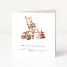 A white greeting card standing upright on a light surface, featuring a watercolour illustration of a Christmas scene with a rocking chair, gifts, books, and a nutcracker. The text reads 'MERRY CHRISTMAS and a happy new year'.