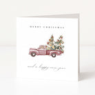 A white Christmas greeting card featuring a watercolour illustration of a vintage pink pickup truck carrying two decorated Christmas trees. The text 'MERRY CHRISTMAS' appears above the truck, and 'and a happy new year' is written below in a cursive font.