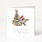 A white Christmas greeting card standing upright on a light grey surface. The front features an illustration of a decorated tree beside a mailbox with a red cardinal perched on top, and the text 'MERRY CHRISTMAS and a happy new year' below.