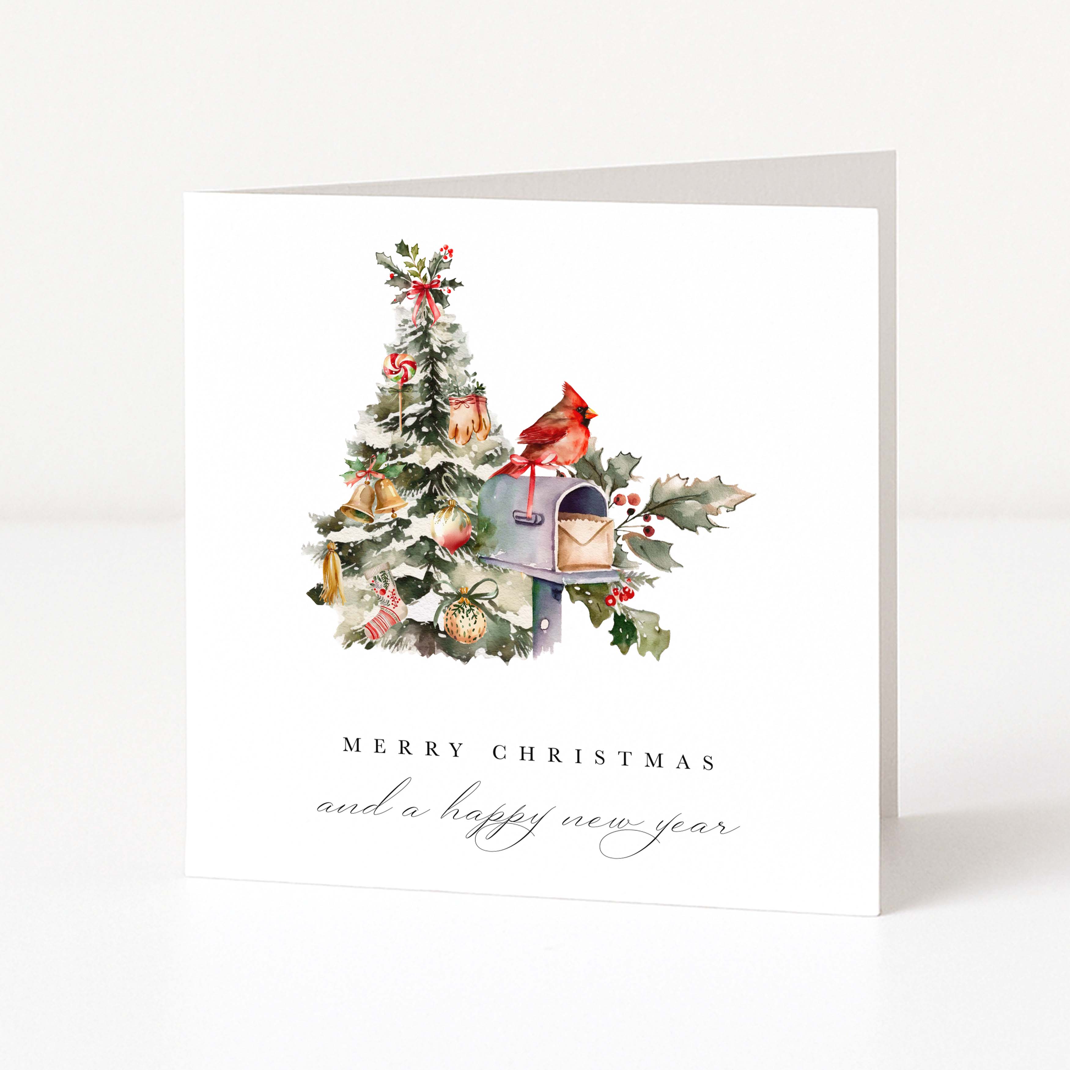 A white Christmas greeting card standing upright on a light grey surface. The front features an illustration of a decorated tree beside a mailbox with a red cardinal perched on top, and the text 'MERRY CHRISTMAS and a happy new year' below.