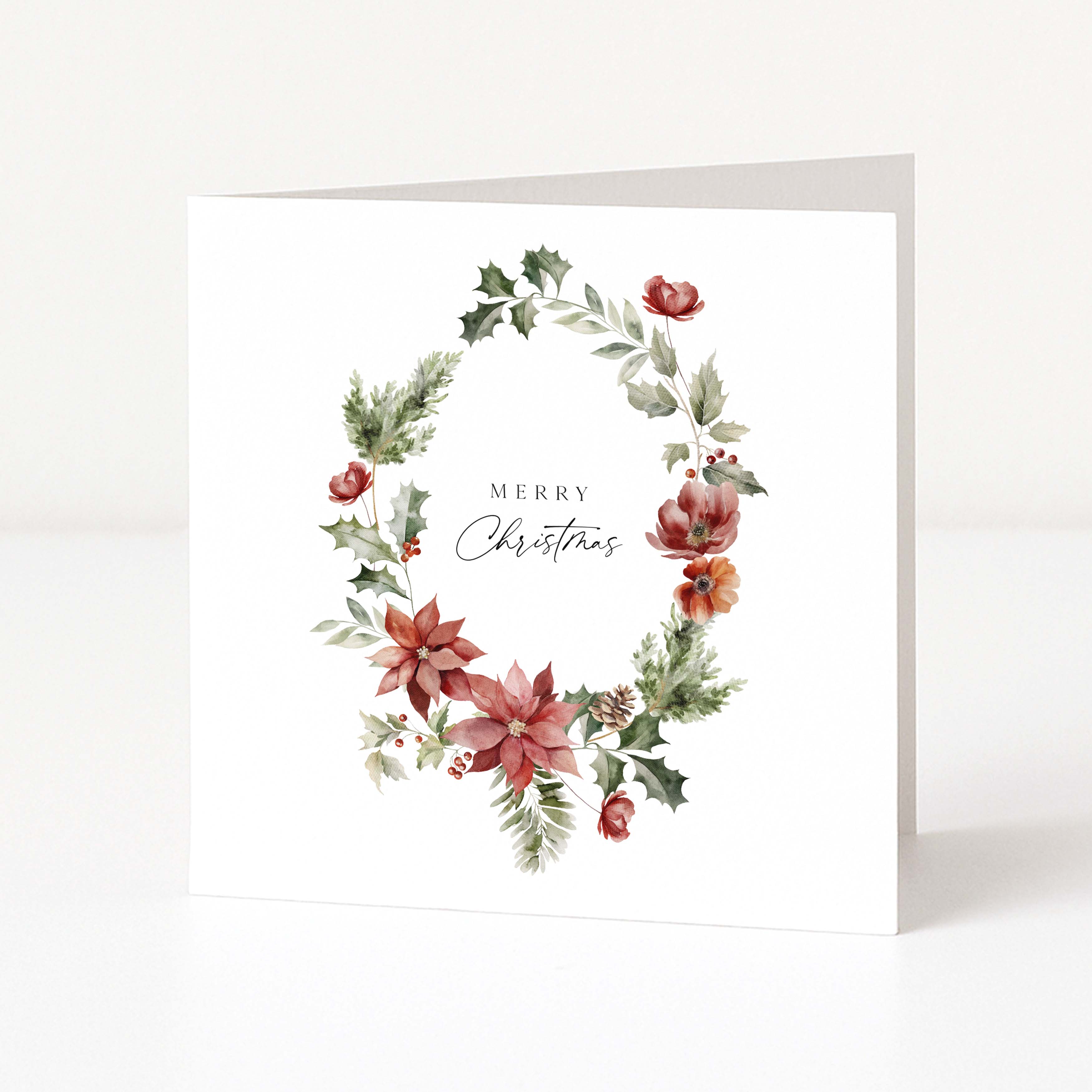 A square white Christmas greeting card standing upright, featuring a watercolour floral wreath with poinsettias, holly, and greenery, plus the words “Merry Christmas” in the centre.