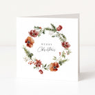 A square white Christmas greeting card standing upright, featuring a watercolour floral wreath with red and orange flowers, green leaves, and small berries around the words “MERRY Christmas” in black script.