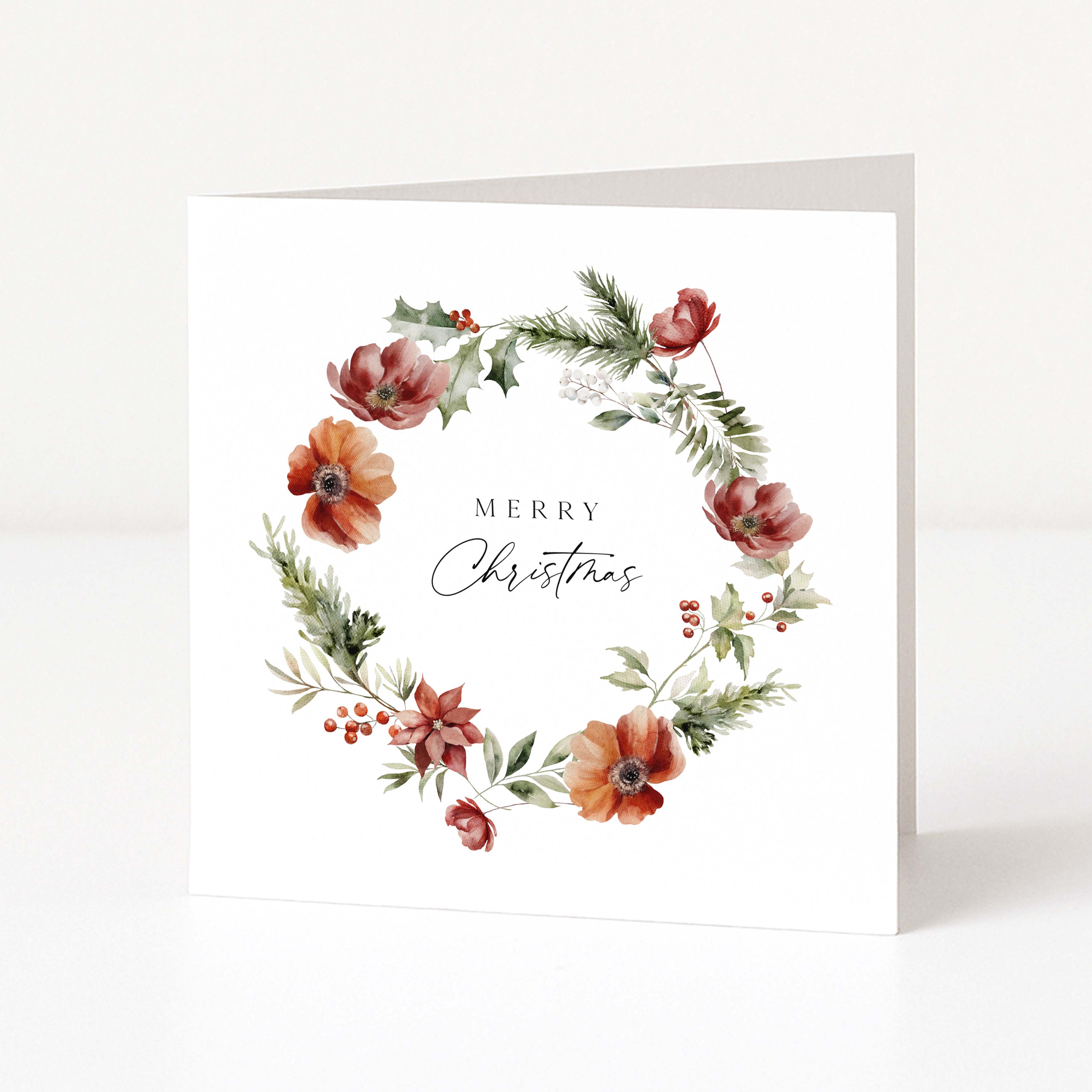 A square white Christmas greeting card standing upright, featuring a watercolour floral wreath with red and orange flowers, green leaves, and small berries around the words “MERRY Christmas” in black script.