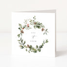 A square white greeting card with a watercolour wreath of green foliage, pinecones, and small red berries around the words 'LET IT SNOW' in black serif and script text, shown standing against a clean white background.