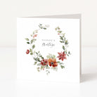 A white greeting card standing upright, featuring a watercolour floral wreath with green leaves, red and orange flowers, and the words 'Season's Greetings' in the centre.