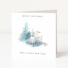 A white square greeting card standing upright on a light surface, printed with the text 'MERRY CHRISTMAS' at the top and 'AND A HAPPY NEW YEAR' at the bottom. The centre shows a soft watercolour illustration of two white deer beside blue-green evergreen trees.