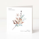 A square white greeting card with a watercolour floral illustration in soft beige, blush, green, and brown tones. The card reads 'MERRY CHRISTMAS' at the top left and 'AND A HAPPY NEW YEAR' at the bottom right, photographed standing against a clean white background.