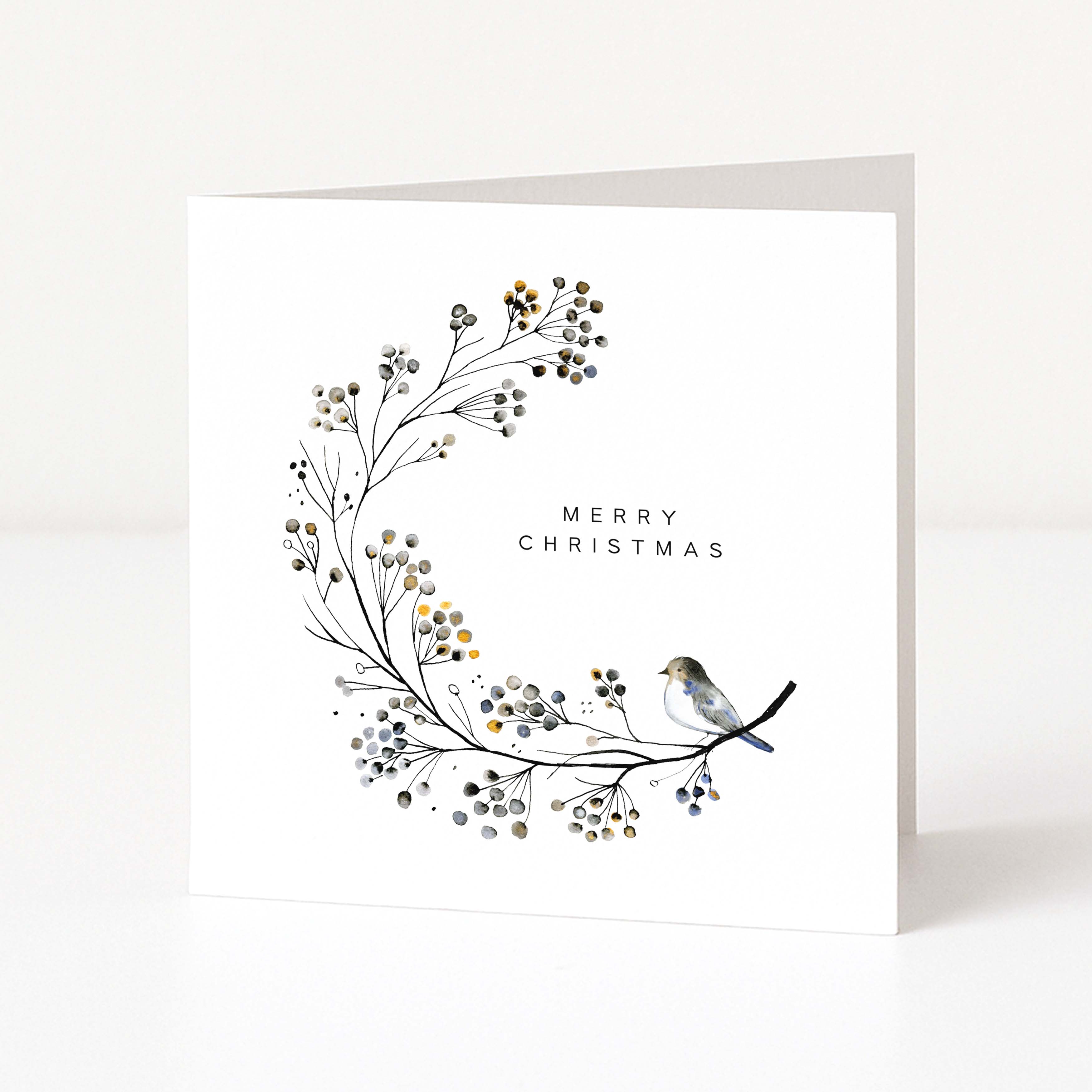 A square white Christmas greeting card standing upright, featuring a delicate watercolour wreath of branches with small berries in grey, black, and muted gold, plus a small bird perched on the right side and the words “MERRY CHRISTMAS” in a simple serif font.