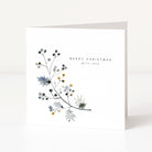 A square white Christmas greeting card standing upright on a white surface, featuring delicate watercolour botanical branches in muted blue, grey, black, and small gold accents, with the text 'MERRY CHRISTMAS WITH LOVE' printed on the front.