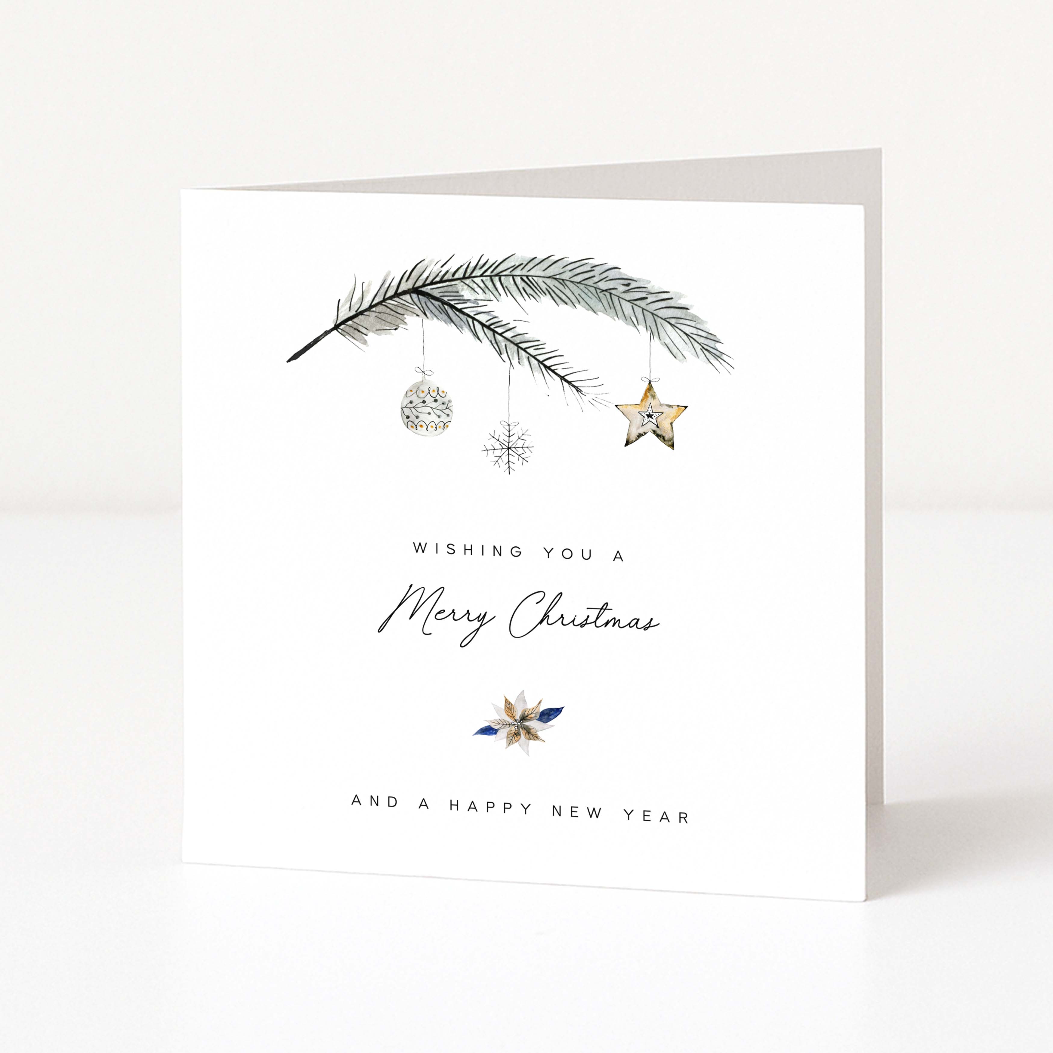 A white Christmas greeting card standing upright on a light surface, printed with a Christmas branch, hanging ornaments, a snowflake, a star, and the text 'Wishing you a Merry Christmas and a Happy New Year'.