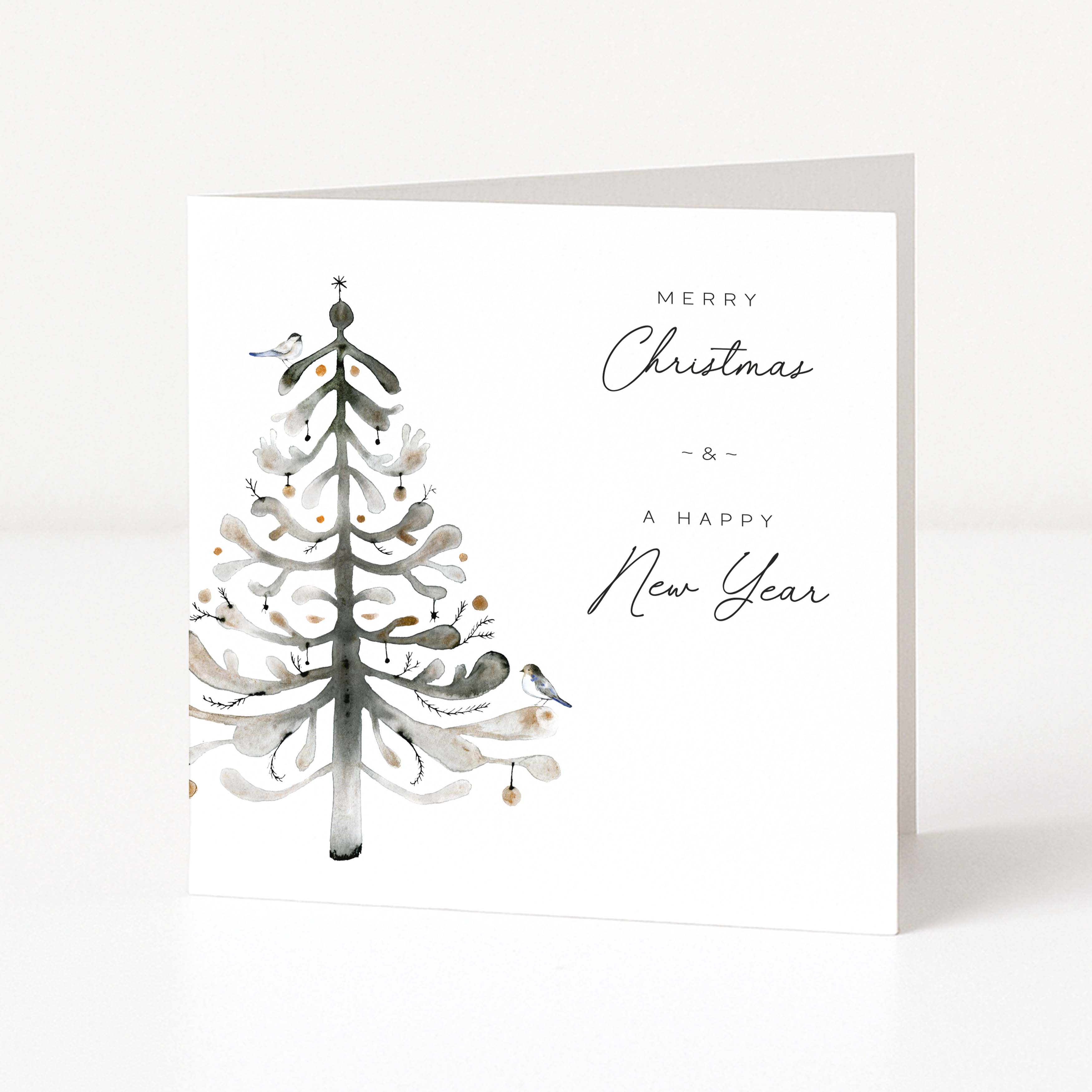 A square white Christmas greeting card standing upright on a white surface, featuring a watercolor-style Christmas tree on the left and the words “MERRY Christmas & A HAPPY New Year” on the right.