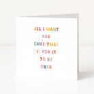 A white anti-Christmas card standing upright on a white surface, with colorful text that reads, 'ALL I WANT FOR CHRISTMAS IS FOR IT TO BE OVER.'.
