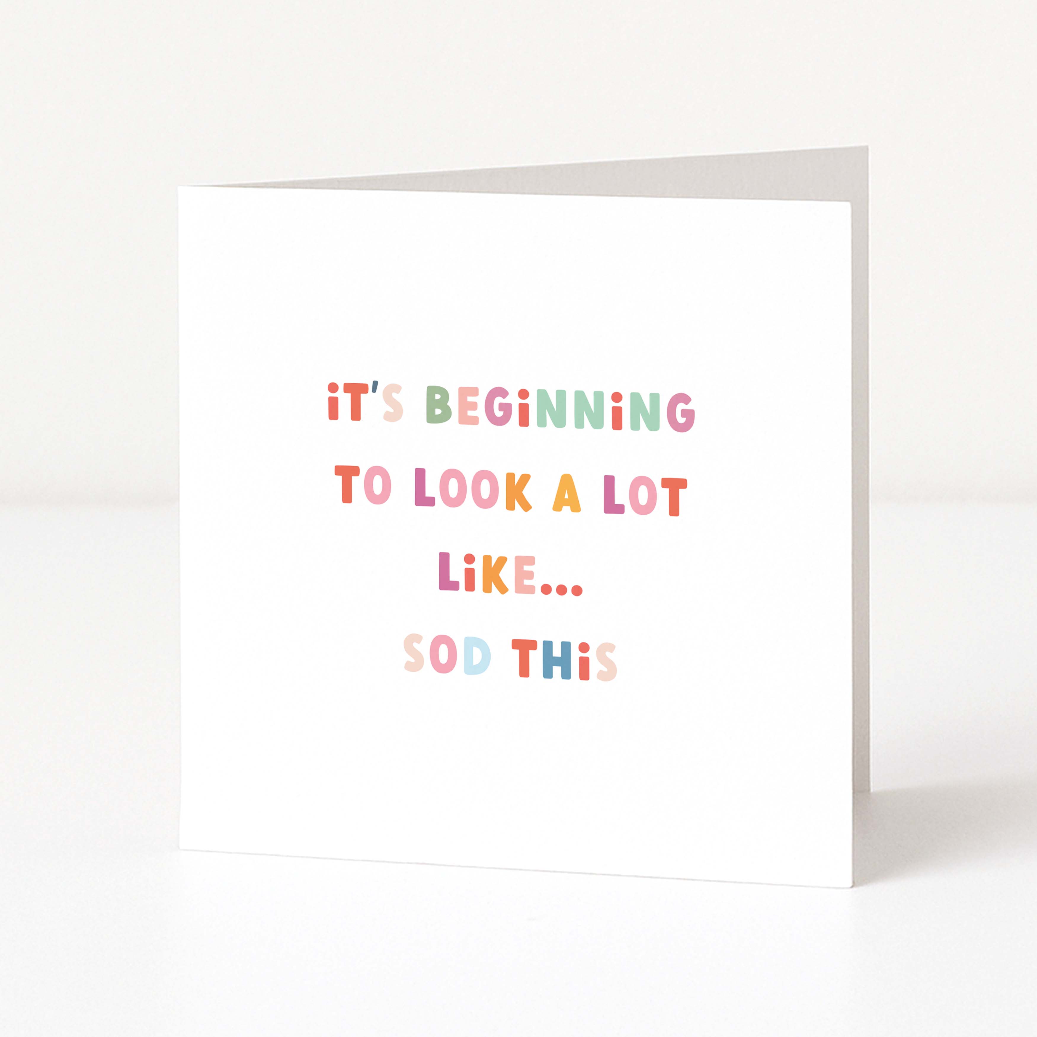 A white greeting card standing upright on a white surface, with pastel-colored text that reads, 'it's BEGINning TO LOOK A LOT LiKE.
