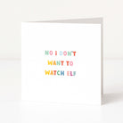A white anti-Christmas card standing upright on a white surface, with the text 'NO i DON'T WANT TO WATCH ELF' printed in small pastel rainbow letters.