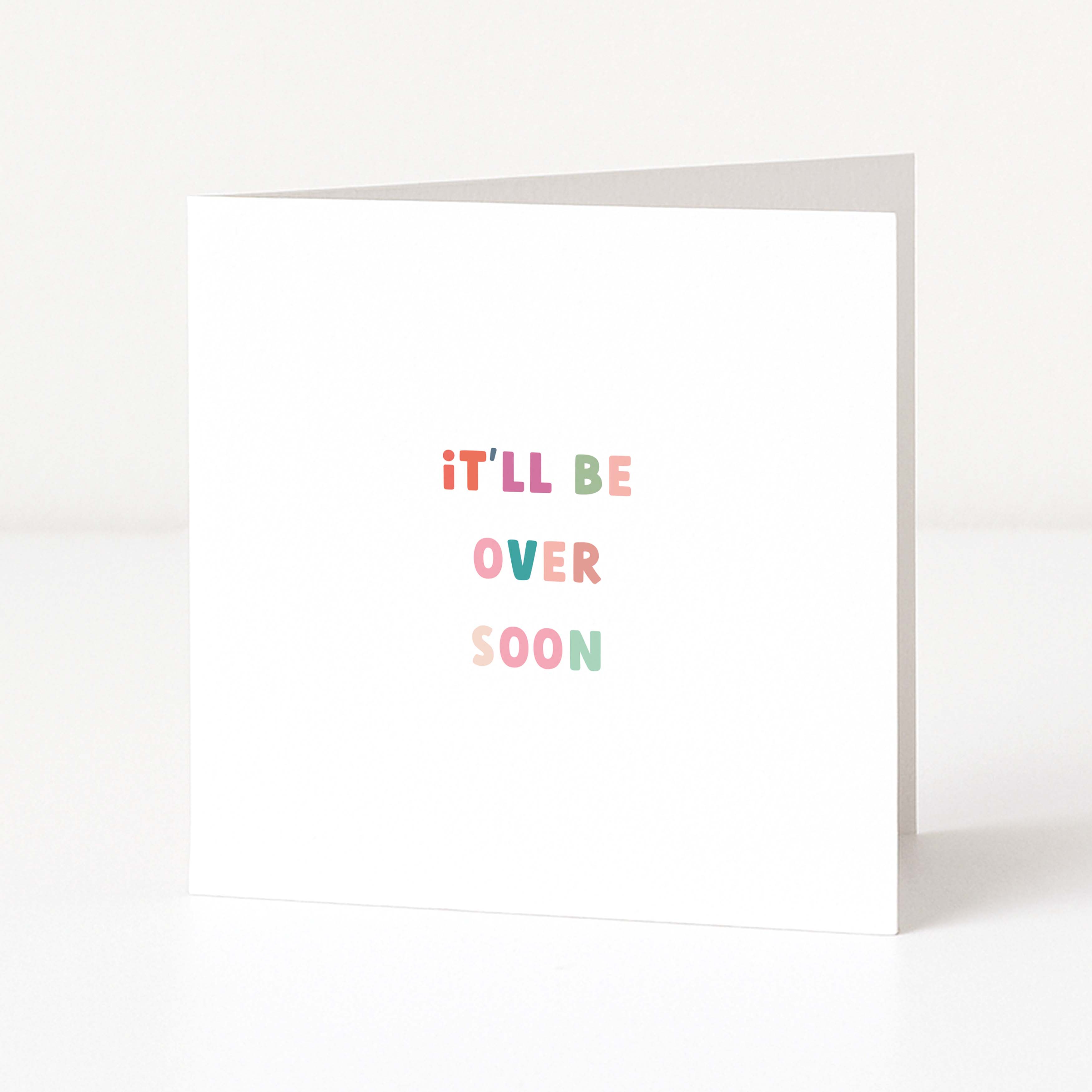 A white anti-Christmas card standing upright on a white surface, with the phrase 'it'LL BE OVER SOON' printed in small pastel letters.