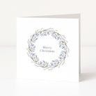 A white square Christmas greeting card standing upright on a white surface, featuring a delicate grey and blue-grey wreath illustration with small yellow accents around the words 'Merry Christmas' in a muted serif font.