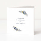 A white Christmas greeting card standing upright on a light surface, with the text 'Wishing you a Merry Christmas and a Happy New Year' centered on the front. Decorative watercolour-style floral sprigs in muted blue-grey and yellow appear near the top and bottom corners.