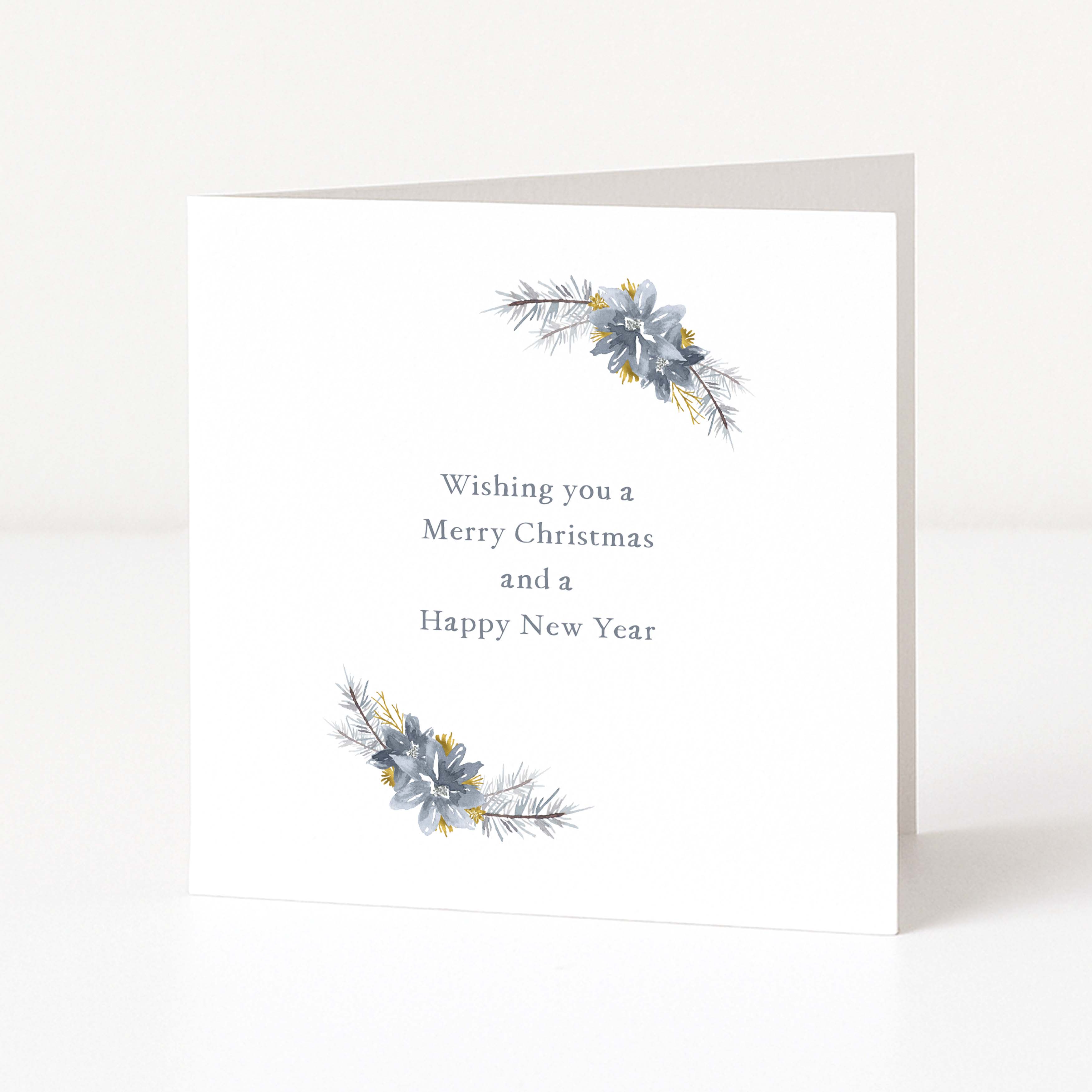 A white Christmas greeting card standing upright on a light surface, with the text 'Wishing you a Merry Christmas and a Happy New Year' centered on the front. Decorative watercolour-style floral sprigs in muted blue-grey and yellow appear near the top and bottom corners.