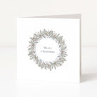 A white square Christmas greeting card standing upright on a white surface, featuring a delicate wreath illustration in muted grey-green and taupe tones with the words 'Merry Christmas' centered inside the wreath.