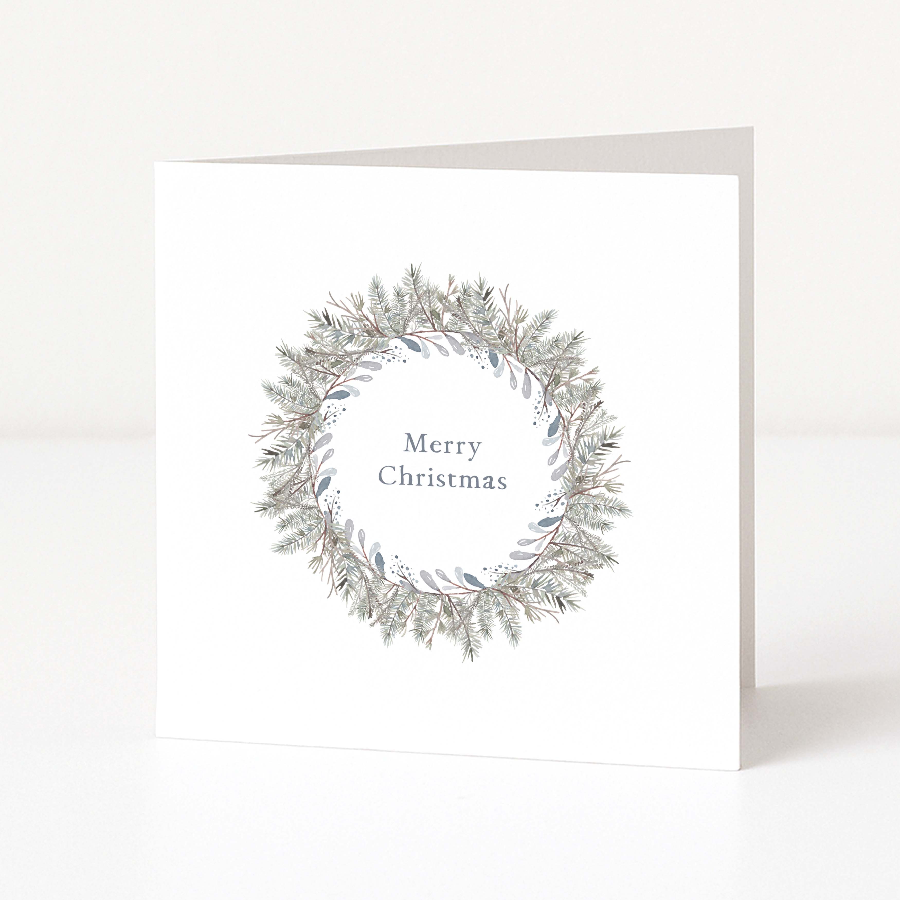 A white square Christmas greeting card standing upright on a white surface, featuring a delicate wreath illustration in muted grey-green and taupe tones with the words 'Merry Christmas' centered inside the wreath.