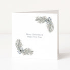 A white Christmas greeting card standing upright on a white surface, with two silver-grey pine branch corner designs and the text 'Merry Christmas & Happy New Year' in the center.