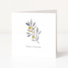 A white square Christmas greeting card standing upright on a white surface, featuring a watercolour-style botanical branch with muted grey-green leaves and small gold berries above the words 'Happy Christmas' in a delicate gray font.