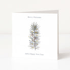 A minimalist white Christmas greeting card standing upright on a white surface, featuring a watercolour-style grey pine branch with small gold dots and the text 'Merry Christmas and a Happy New Year'.