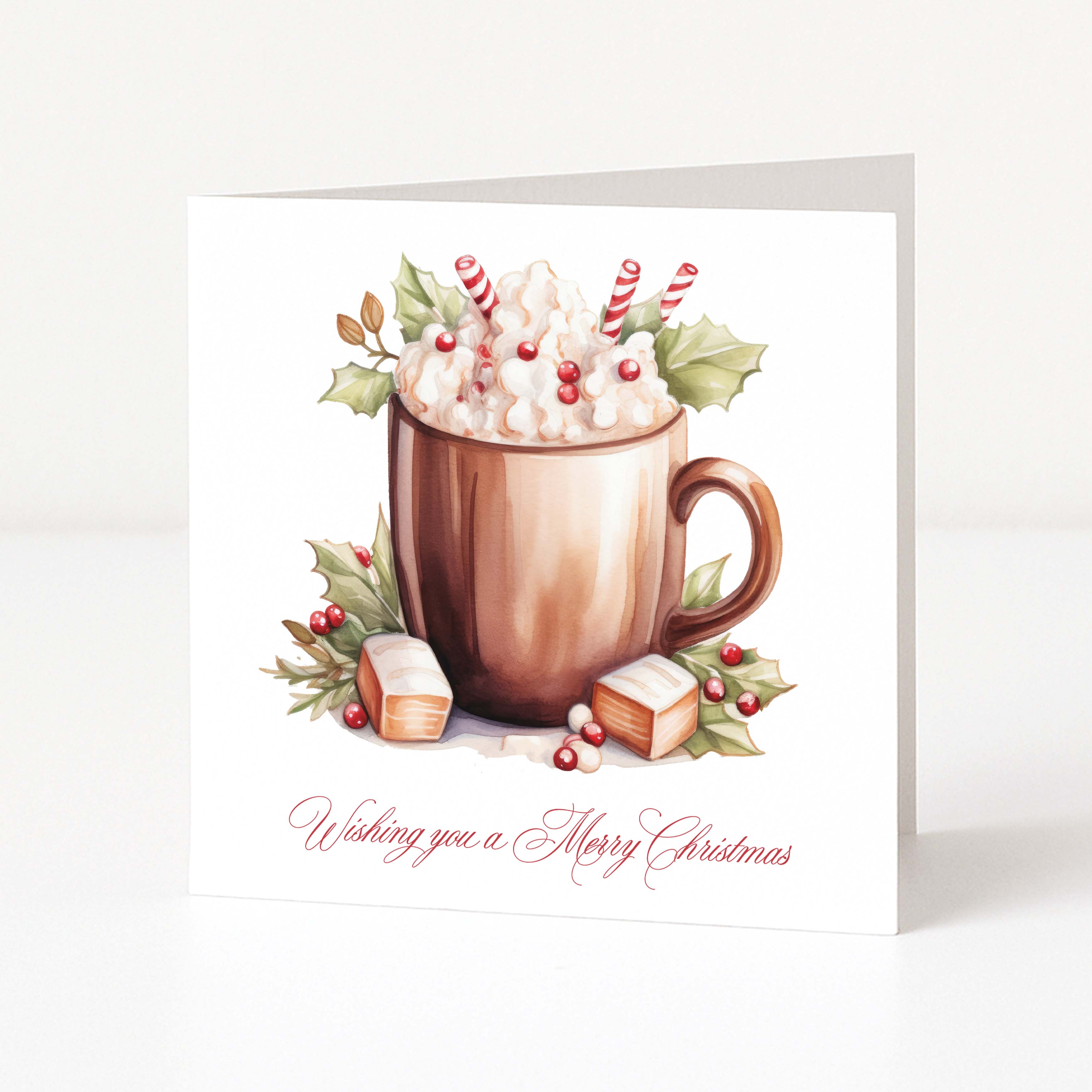 A square Christmas greeting card featuring an illustration of a hot chocolate mug topped with whipped cream, candy canes, holly leaves, and marshmallows, with the text 'Wishing you a Merry Christmas' in red script at the bottom.