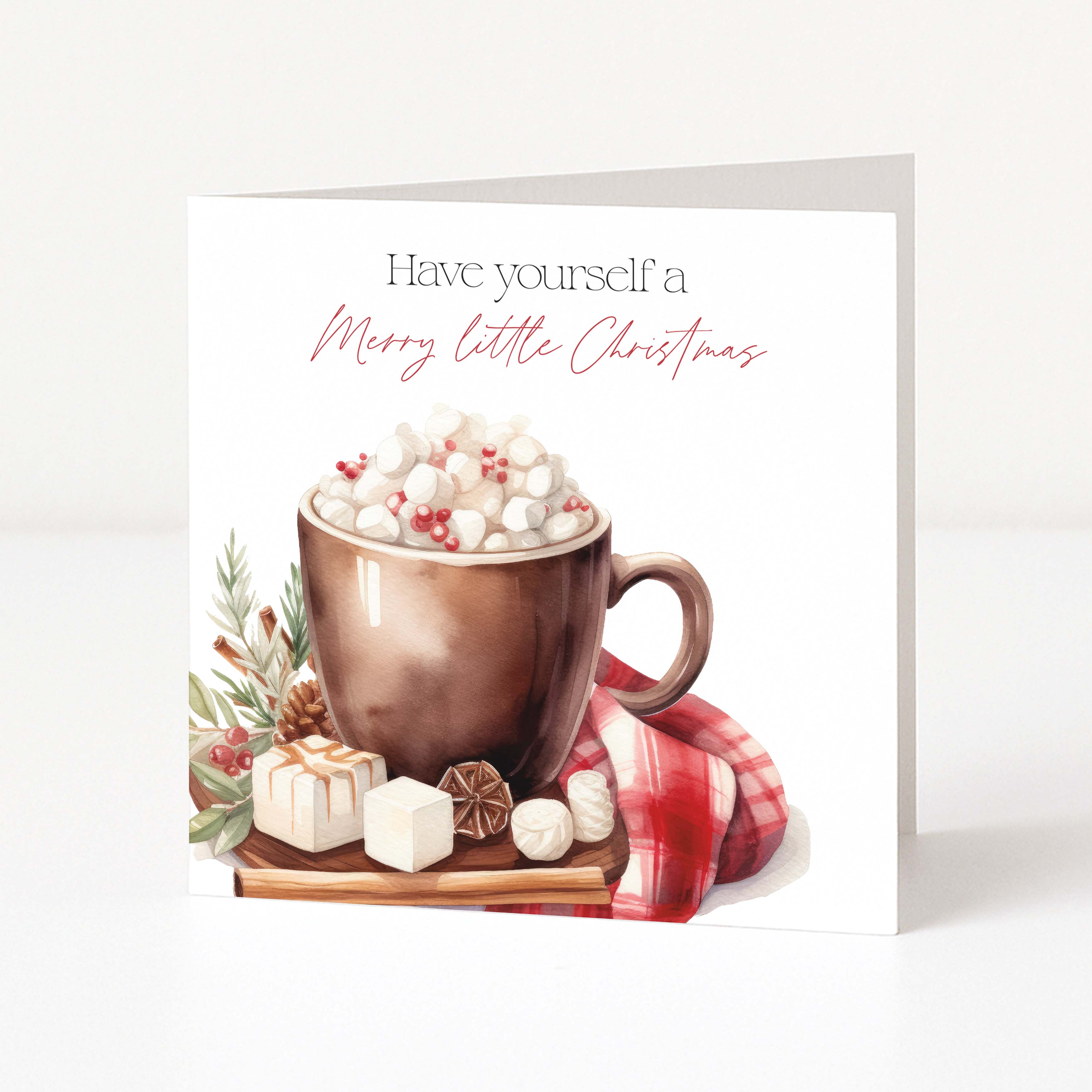 A square Christmas greeting card standing upright on a white surface. The card features the text 'Have yourself a Merry little Christmas' above an illustration of a copper mug filled with marshmallows, wrapped gifts, and a red plaid cloth.