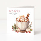 A square Christmas greeting card standing upright on a white surface, featuring a watercolour-style illustration of a mug filled with hot chocolate, marshmallows, cinnamon sticks, and holiday greenery. The card reads “COMFORT and Joy” in red and grey lettering.