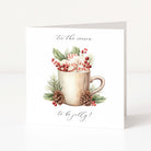 A square white Christmas greeting card standing upright on a light grey surface, featuring a watercolour-style illustration of a beige mug filled with whipped cream and candy canes, surrounded by green leaves, red berries, pinecones, and the phrases 'for the season' and 'to be jolly!'.