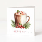 A square white Christmas greeting card standing upright on a light grey surface. The front features a watercolour-style illustration of a hot mug with cocoa, green holly leaves, red berries, and a striped candy cane, with the text 'HAVE A HOLLY JOILY CHRISTMAS' below.