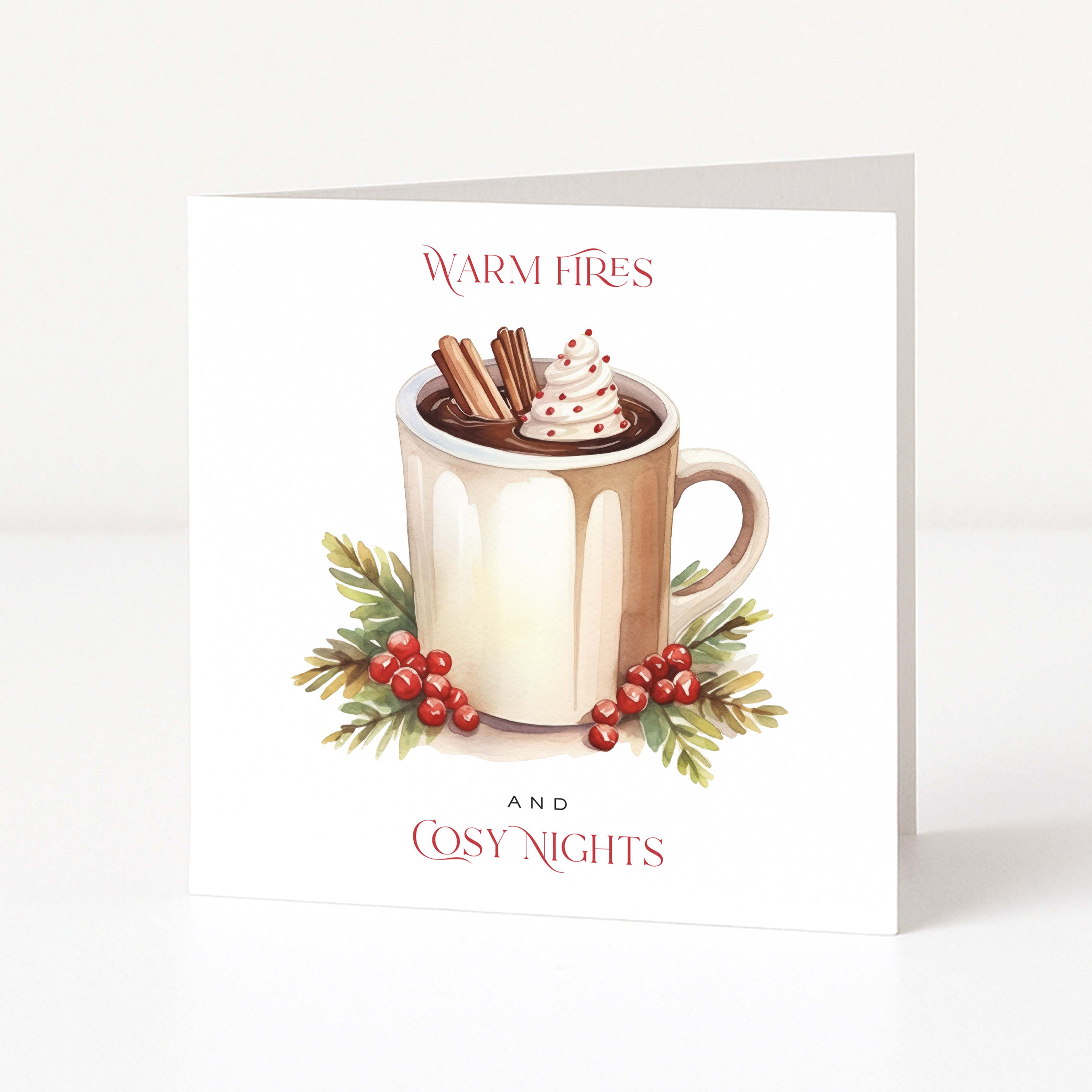 A square Christmas greeting card standing upright on a white surface against a light neutral background. The front of the card features an illustration of a mug filled with hot cocoa or coffee, topped with whipped cream and cinnamon sticks, surrounded by green leaves and red berries.