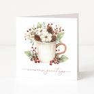 A white Christmas greeting card standing upright on a light surface, featuring a watercolour-style illustration of a white mug filled with cotton bolls, pinecones, green leaves, and red berries, with the words 'season's greetings' in a rose-gold script at the bottom.