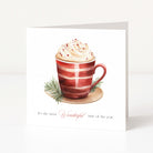 A square Christmas greeting card featuring a watercolor illustration of a red-and-white striped mug filled with whipped cream and holiday sprigs, with the text 'It's the most Wonderful time of the year' printed below on a white background.