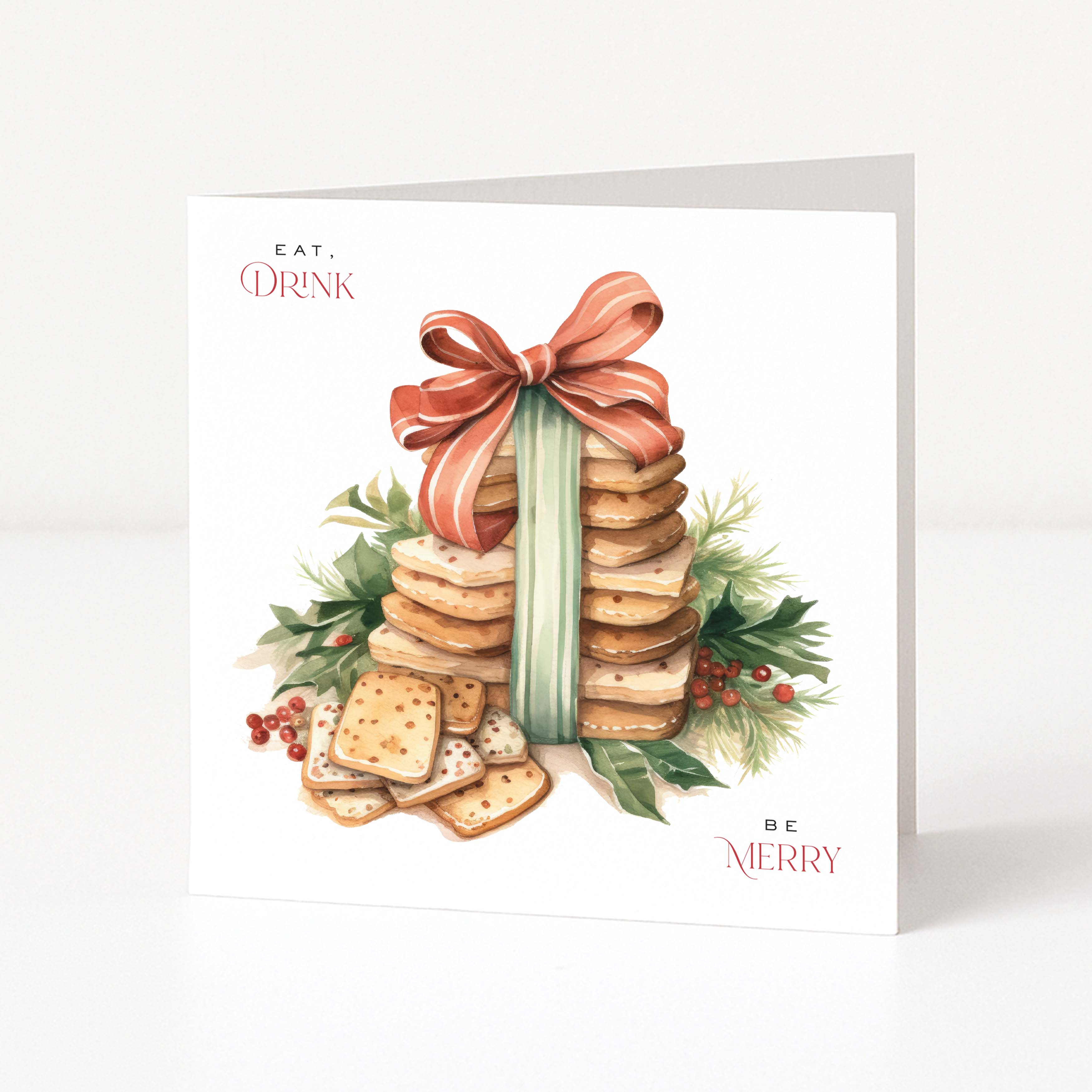A square white Christmas greeting card standing upright on a white surface, featuring a watercolor illustration of stacked cookies and crackers tied with a large coral ribbon, surrounded by green holly leaves and small red berries. The card has the words 'EAT.DRINK, BE MERRY'