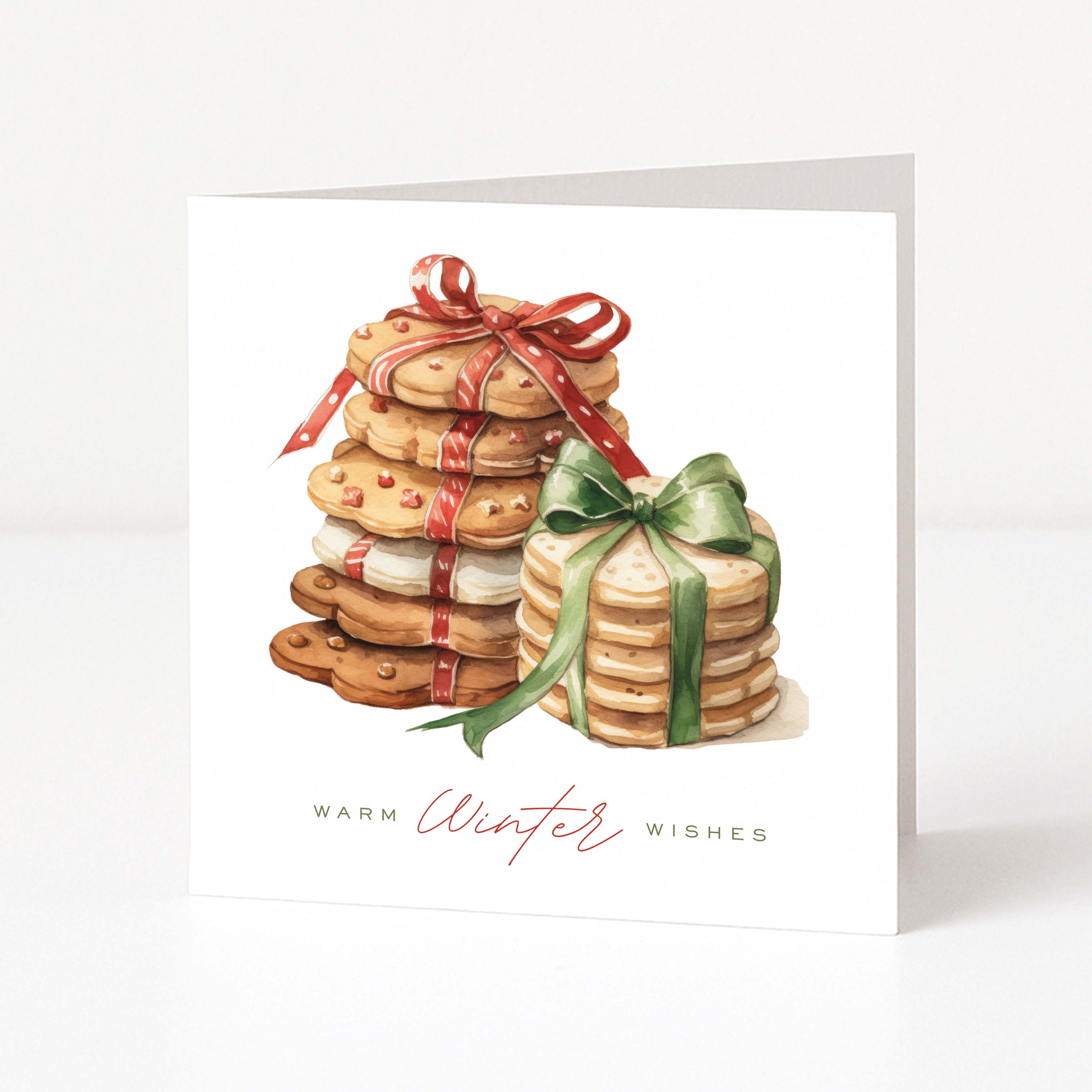 A square white greeting card with a white background featuring an illustration of stacked cookies, one wrapped in a red ribbon and one in a green ribbon, with the text 'WARM Winter Wishes' printed below.