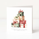 A square white Christmas greeting card standing upright on a white surface, featuring a watercolor illustration of stacked Christmas presents in green, red, beige, and cream tones, with the text 'wishing you a merry christmas and a happy new year' below.