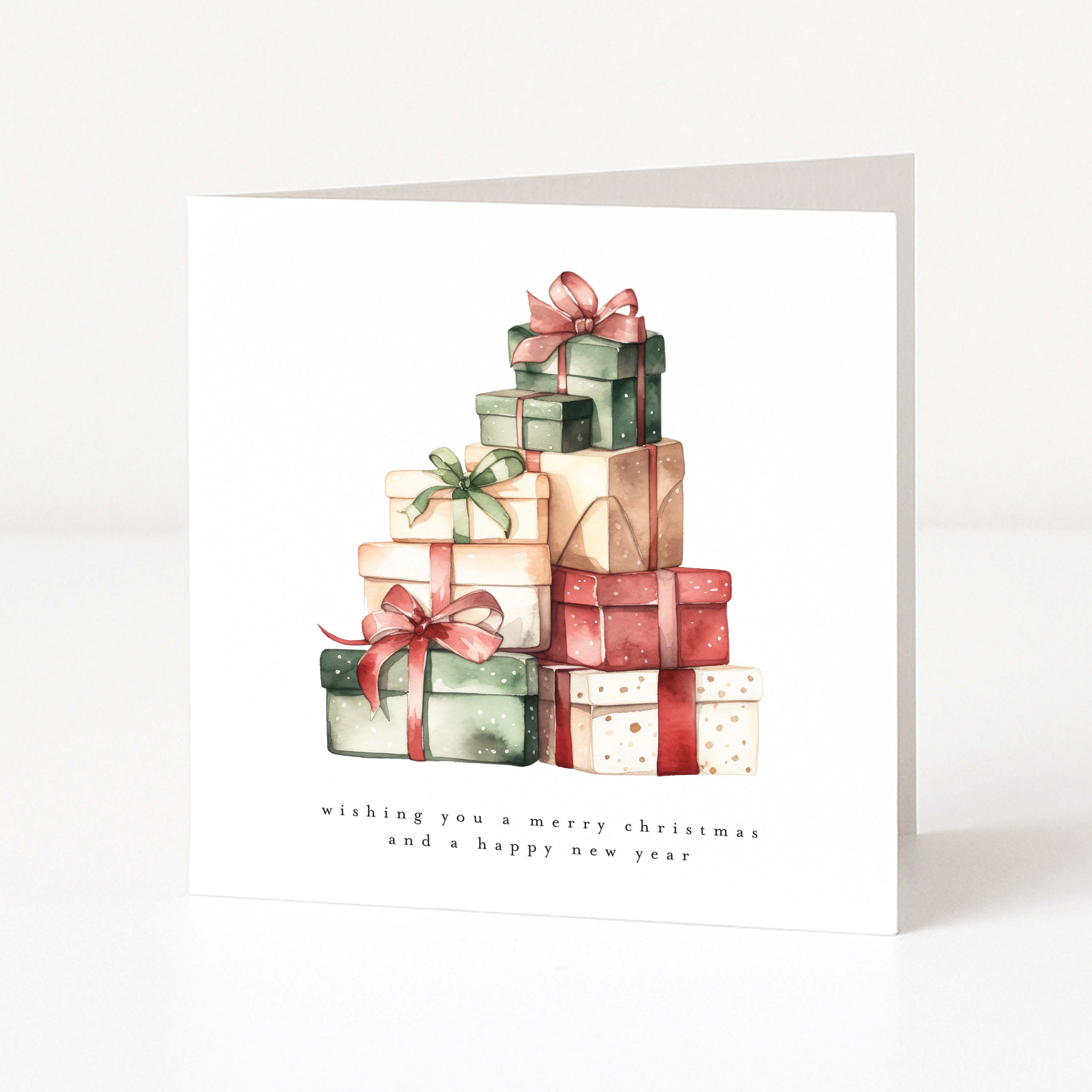 A square white Christmas greeting card standing upright on a white surface, featuring a watercolor illustration of stacked Christmas presents in green, red, beige, and cream tones, with the text 'wishing you a merry christmas and a happy new year' below.