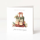 A white Christmas greeting card standing upright on a light surface, printed with the words 'Season's Greetings' and 'from our home to yours' and featuring an illustrated stack of wrapped Christmas presents with greenery accents.