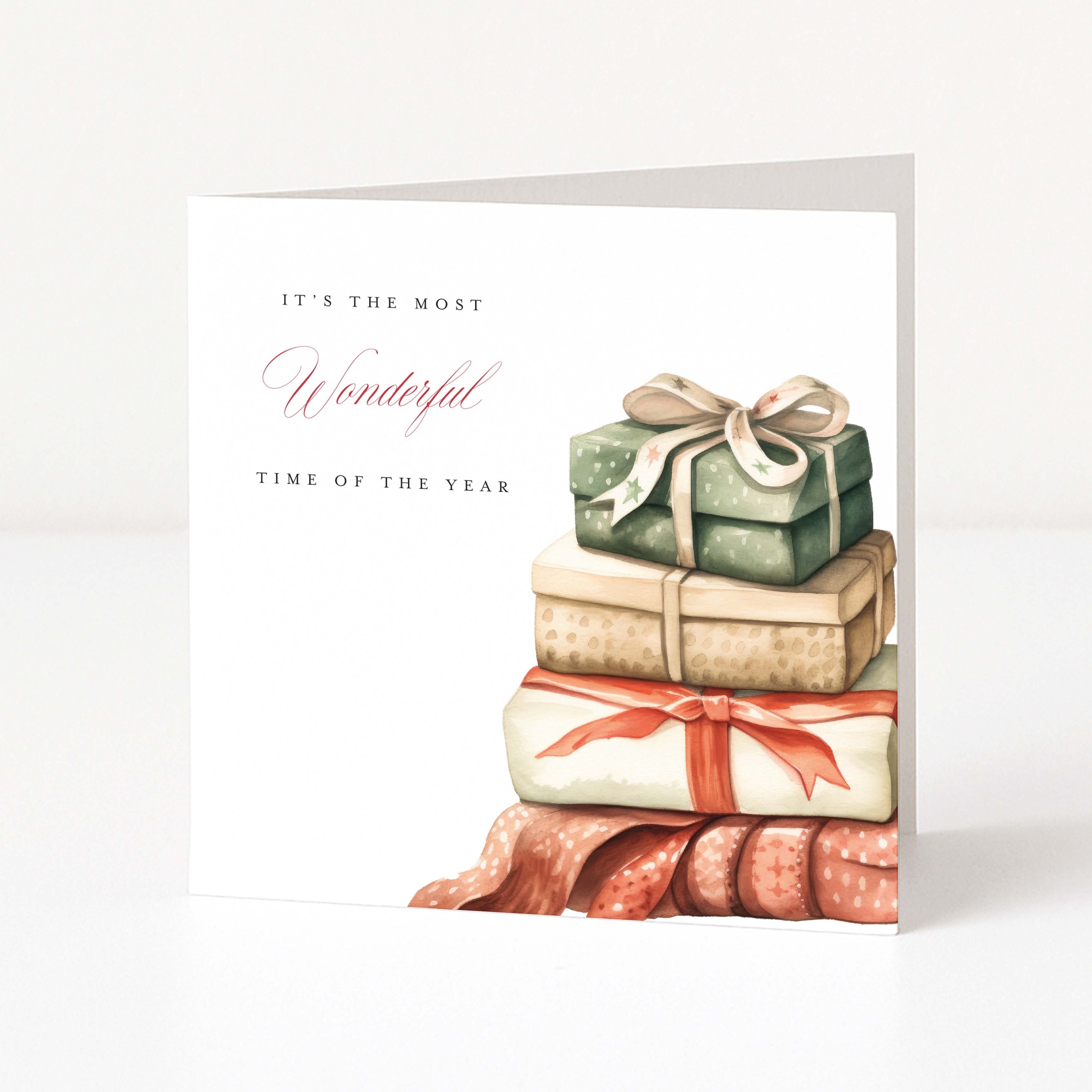 A square Christmas greeting card shown standing upright against a light neutral background. The card has a white base with elegant text reading 'IT'S THE MOST Wonderful TIME OF THE YEAR' and an illustration of stacked wrapped gift boxes in muted green, beige, cream, and rust tones with ribbon bows.